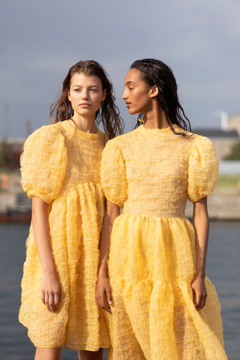 两个女孩分别穿黄色薄纱宽松连衣裙，配湿发，站在河边笑着