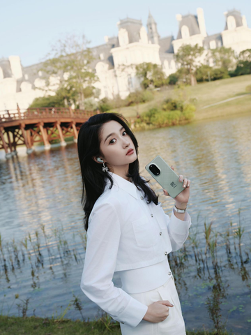 a person holding a smartphone near a body of water with a historical building in the background