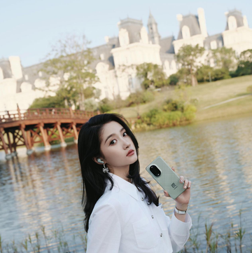a person holding a smartphone near a body of water with a historical building in the background a person holding a smartphone near a body of water with a historical building in the background