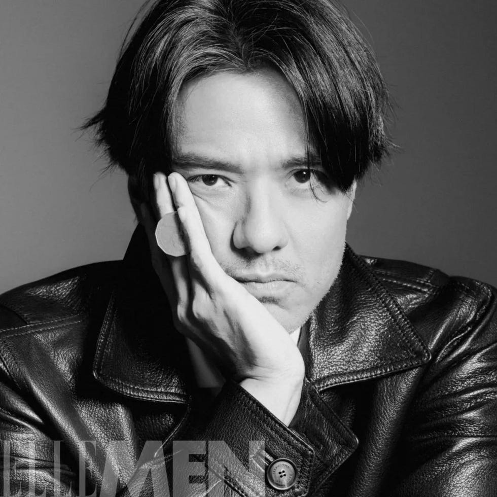 a person wearing a black leather jacket seated with a hand propping up their chin
