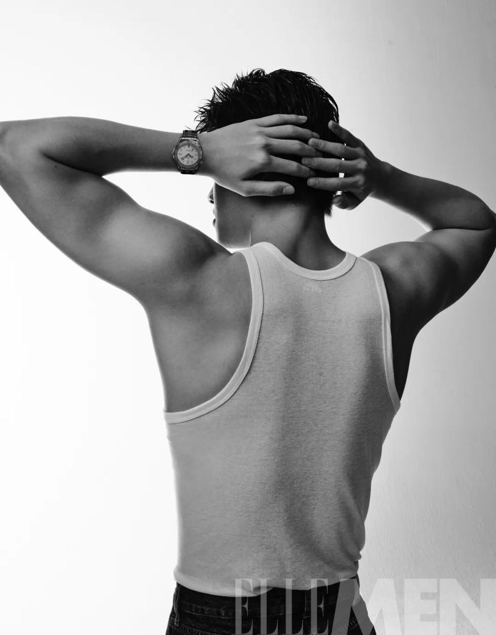 a person with slickedback hair wearing a sleeveless shirt viewed from behind adjusting their hair