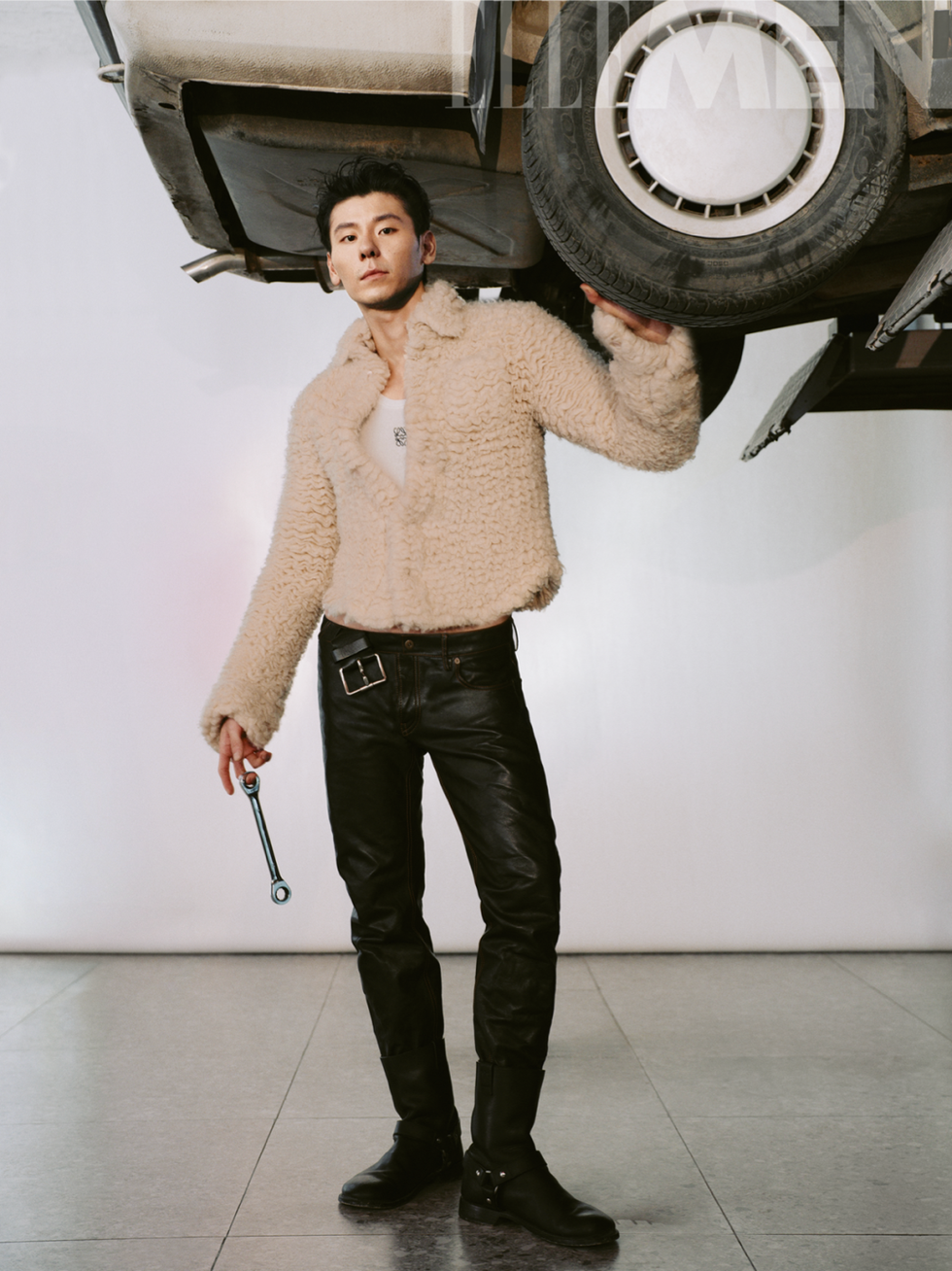 person holding a wrench under an elevated car dressed in warm attire