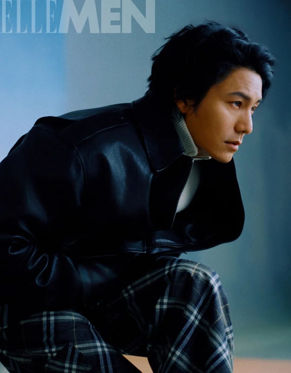 a person wearing a black leather jacket and plaid pants posed in a crouched position