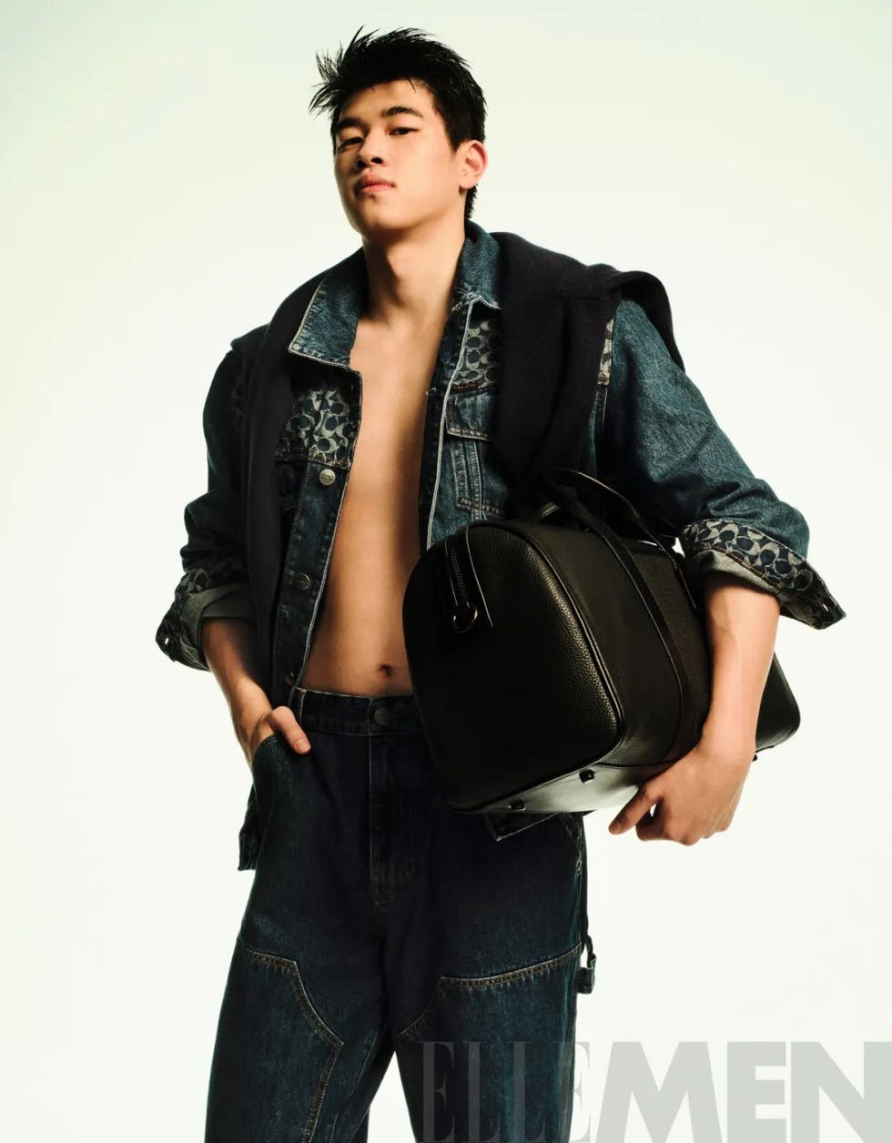 a model poses with a black bag wearing denim clothing