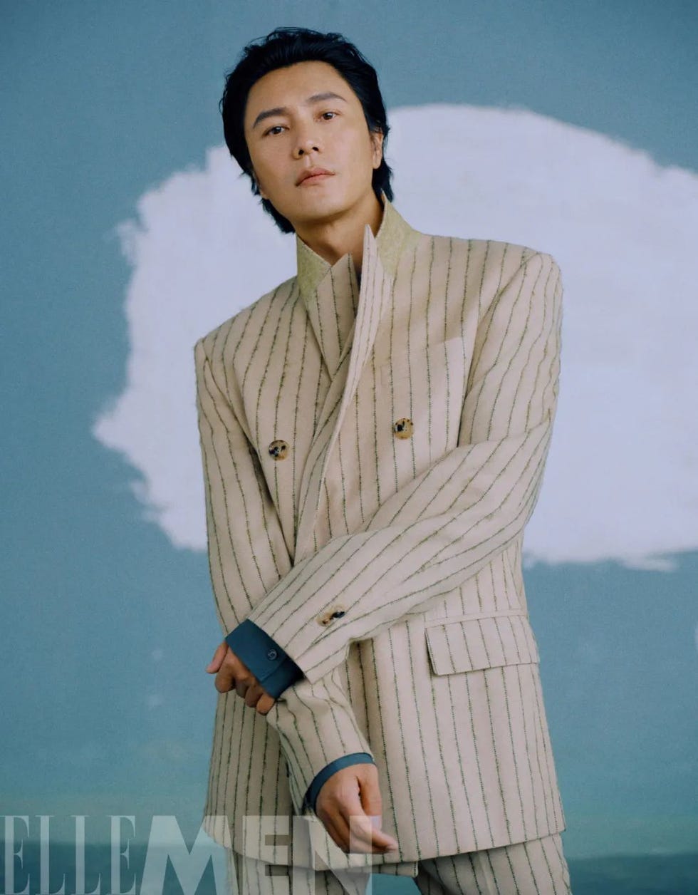 a person wearing a stylish striped suit stands with arms crossed against a soft abstract background