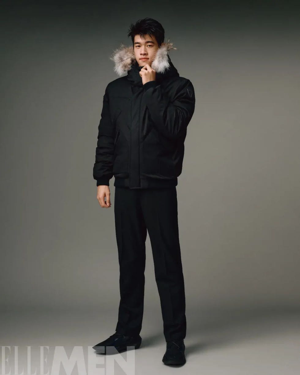 man wearing a black parka and pants standing indoors