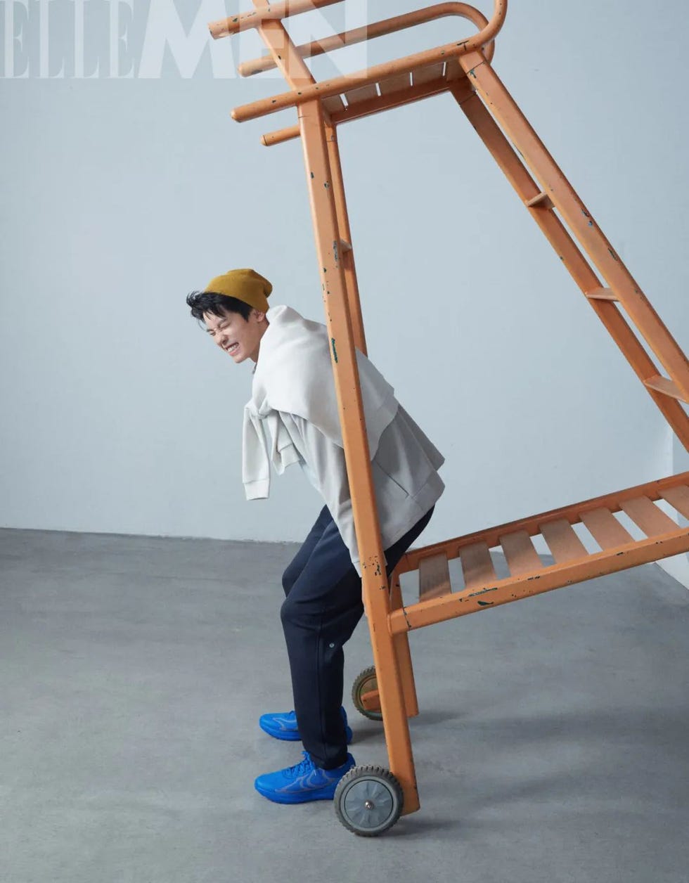 a person in a casual outfit is positioned under an orange ladder creating an interesting pose