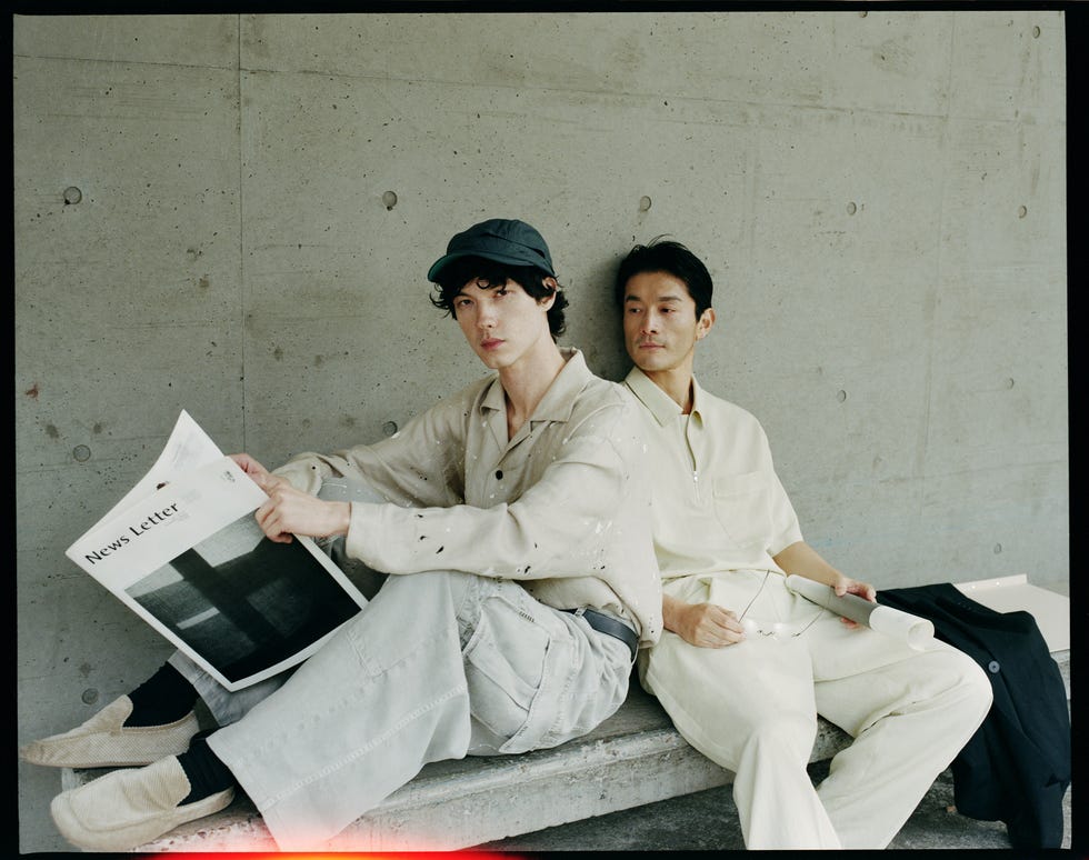 two individuals seated on a bench engaging with a newsletter and a rolled document