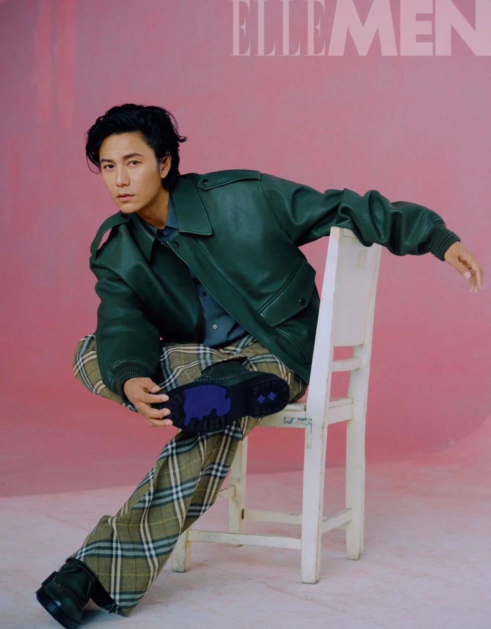 fashion portrait featuring a seated individual wearing a green leather jacket and checked pants