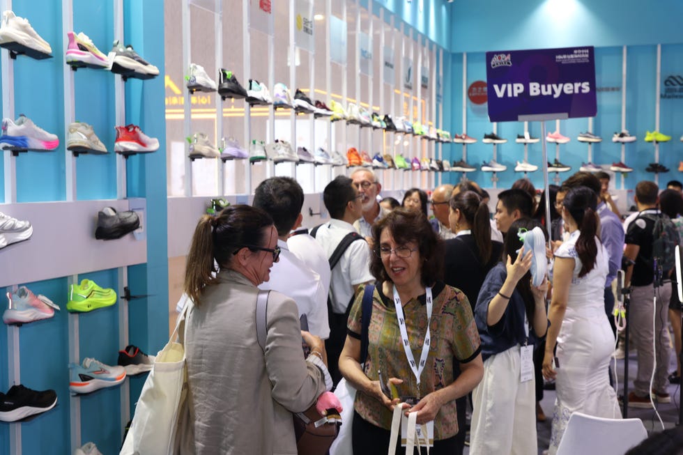 group of individuals at a trade event examining various sneaker models displayed on a wall