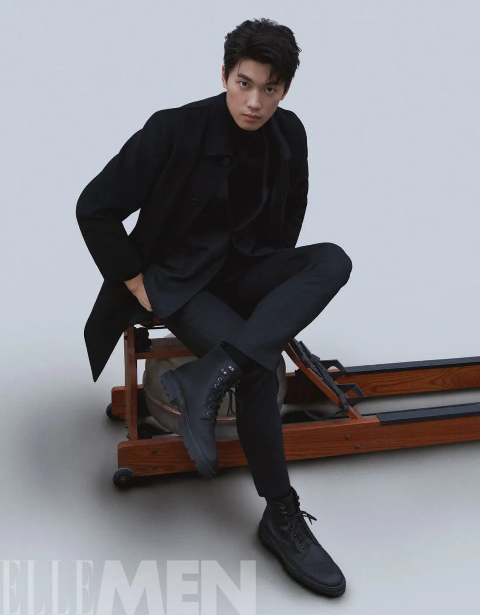 a figure seated on a bench with a wooden frame showcasing a stylish black outfit and boots