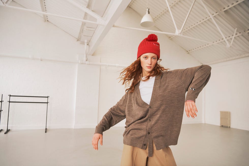 person wearing a red hat and brown cardigan in an empty studio space