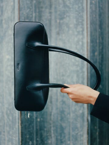 hand holding a sleek black leather bag with two handles