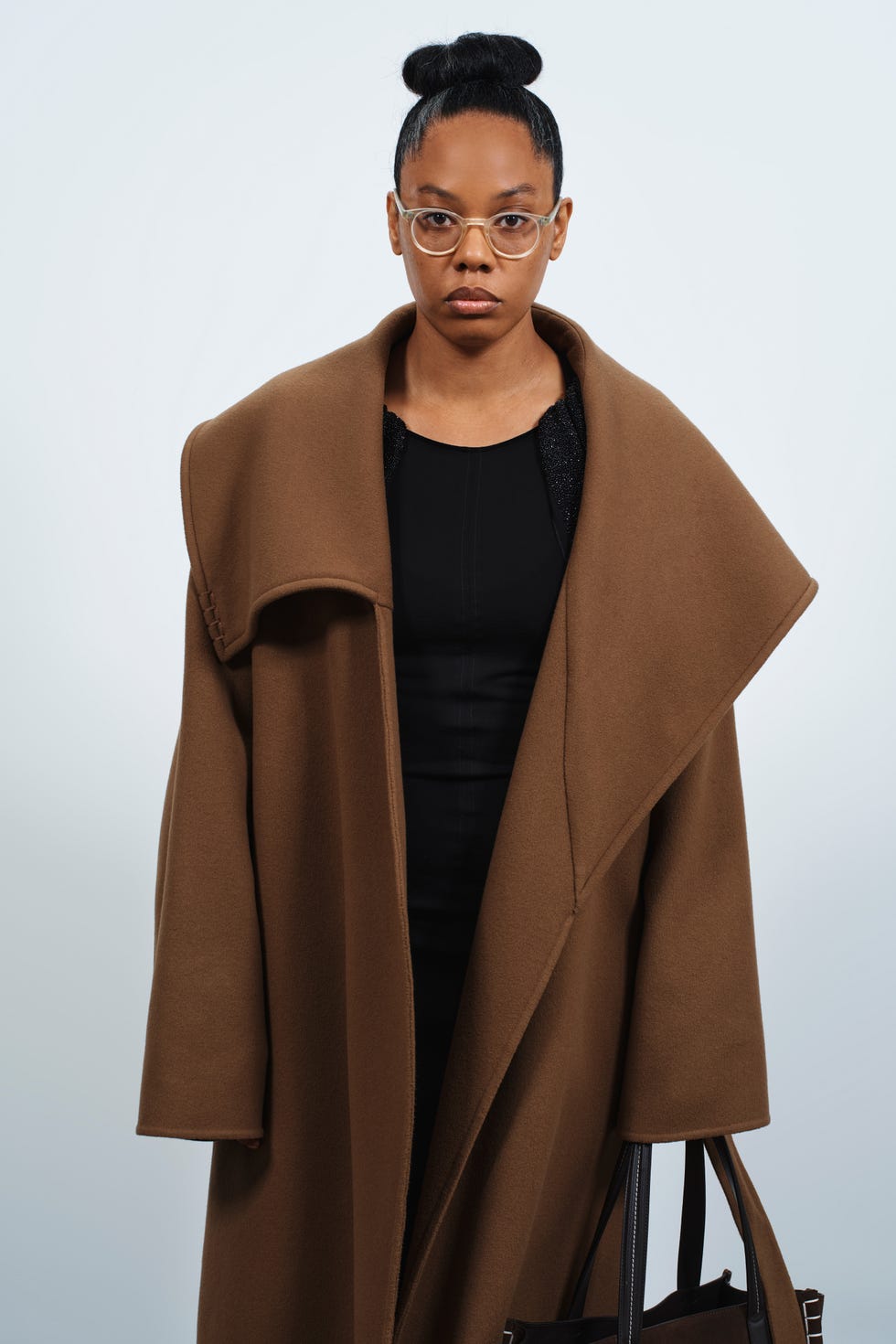 a model showcasing a stylish outfit consisting of a brown overcoat and black dress carrying a handbag