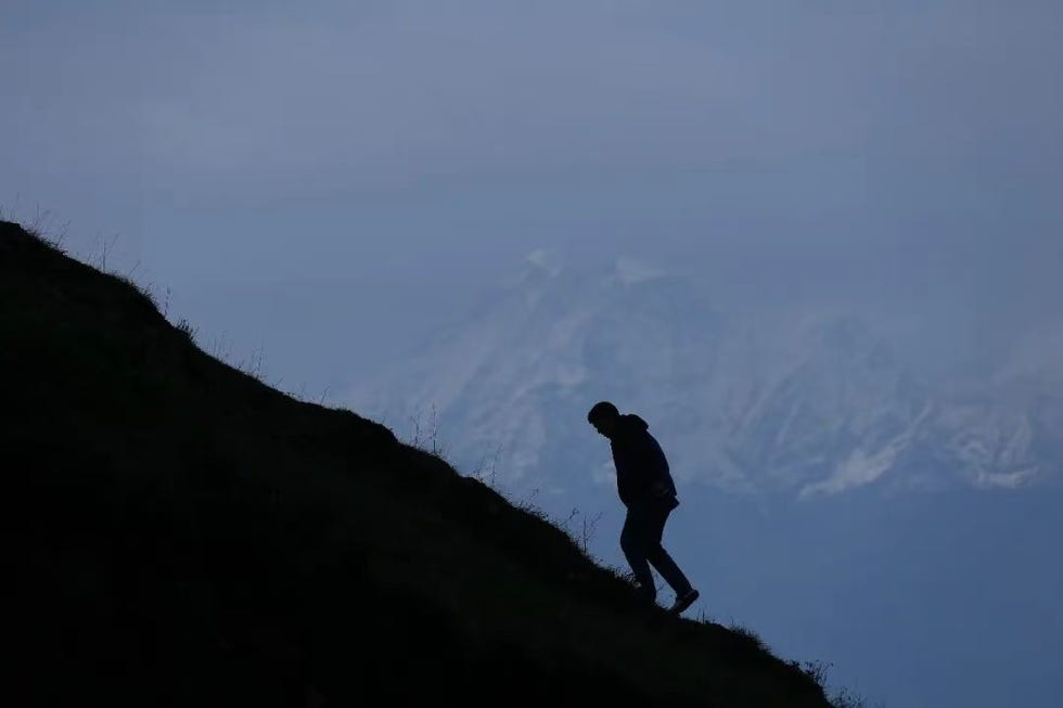 silhouette of a person hiking up a slope with mountains in the background