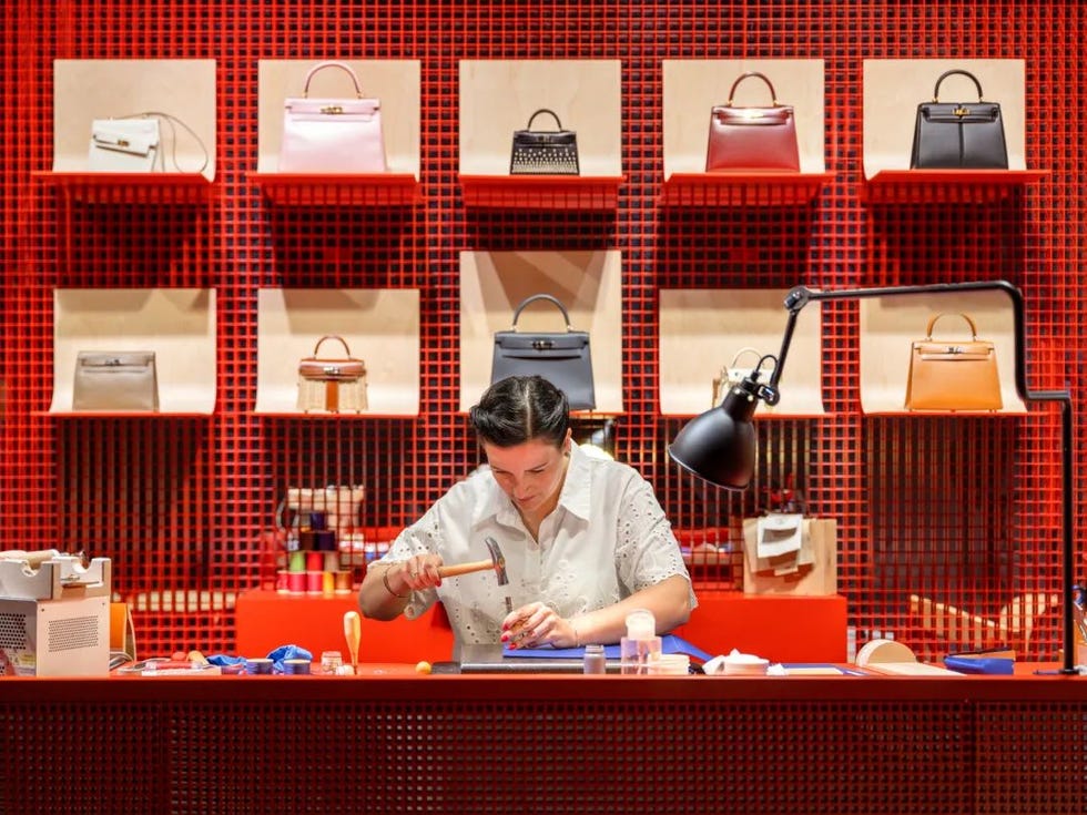 artisan working on handbag craftsmanship with various bags displayed in the background