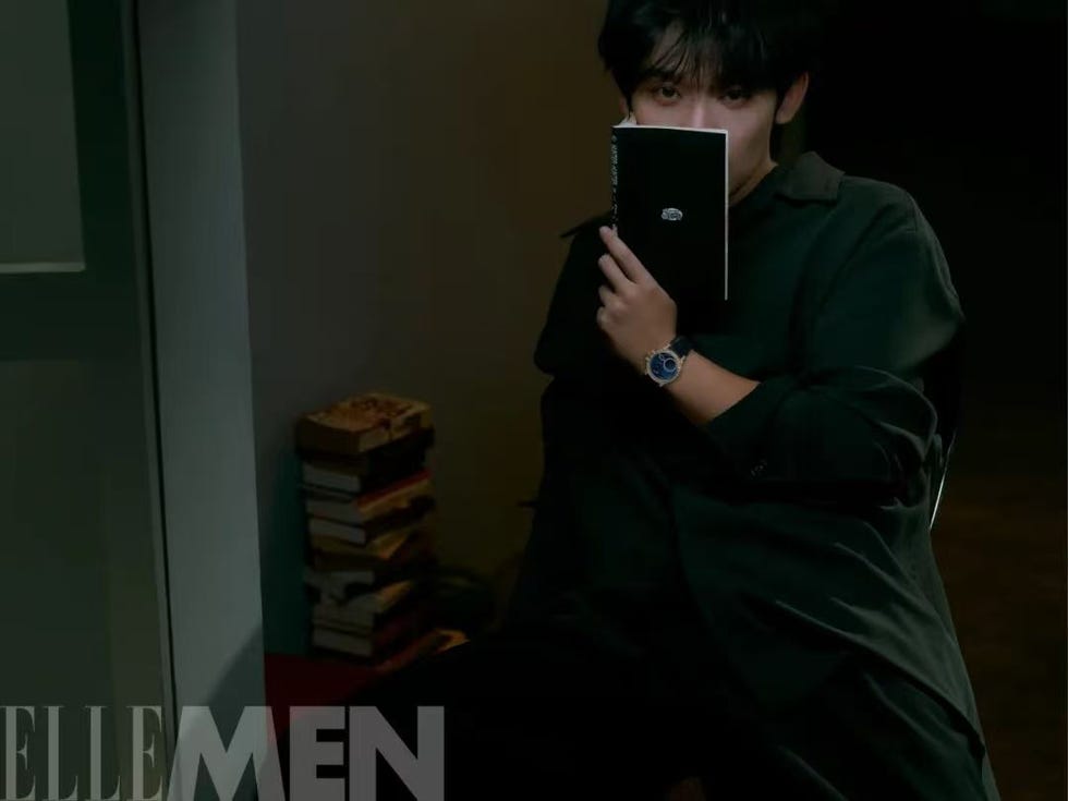 man holding a book in a dimly lit room with a stack of books nearby