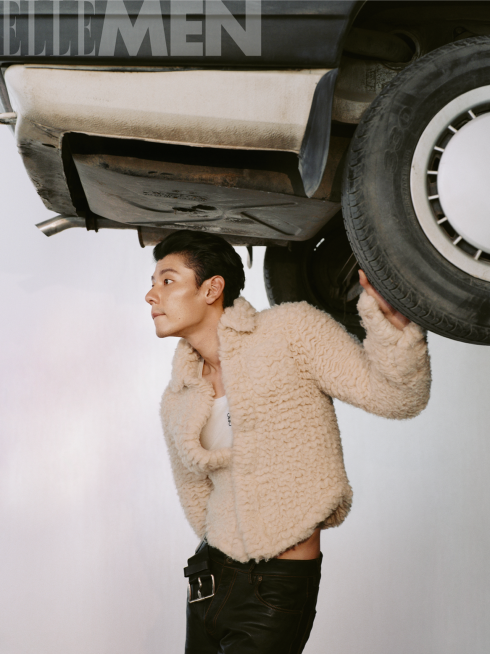a person lifting a vehicle from underneath while wearing a textured beige jacket