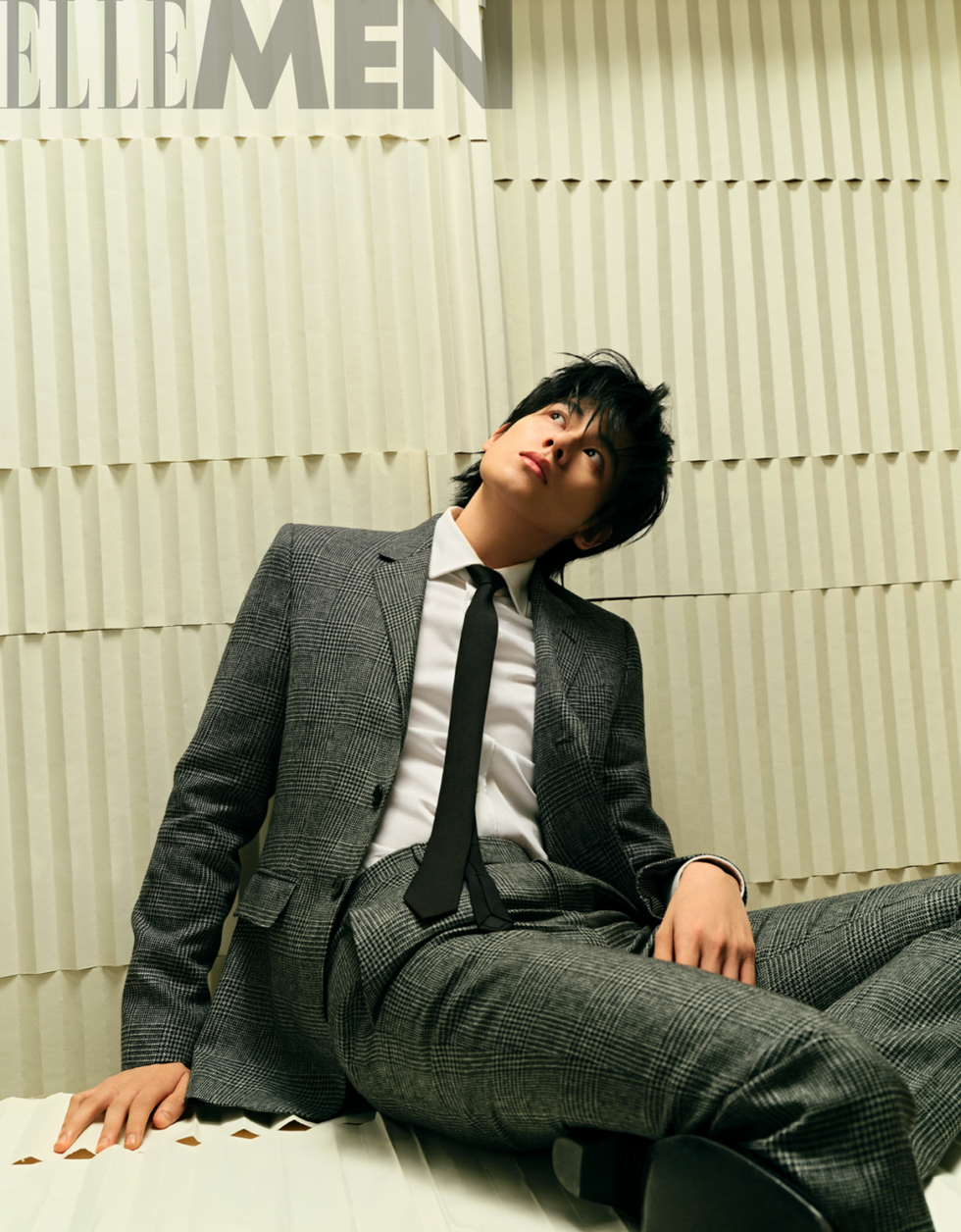 a person in a stylish gray checkered suit reclines on a textured surface