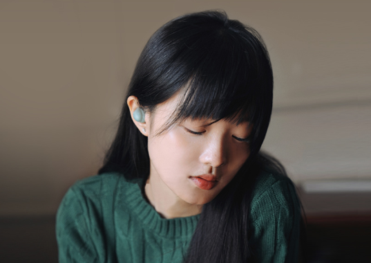person wearing earbuds with long dark hair seated indoors