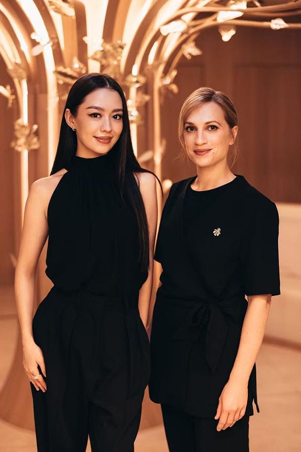 two individuals in black outfits standing against a stylish background