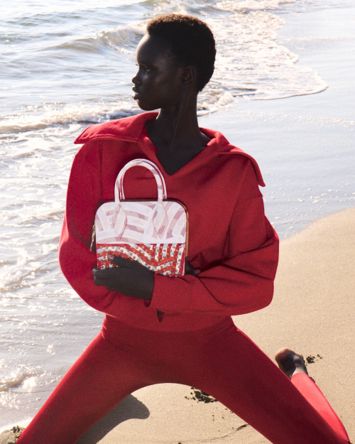 model wearing a red outfit holding a stylish handbag on the beach