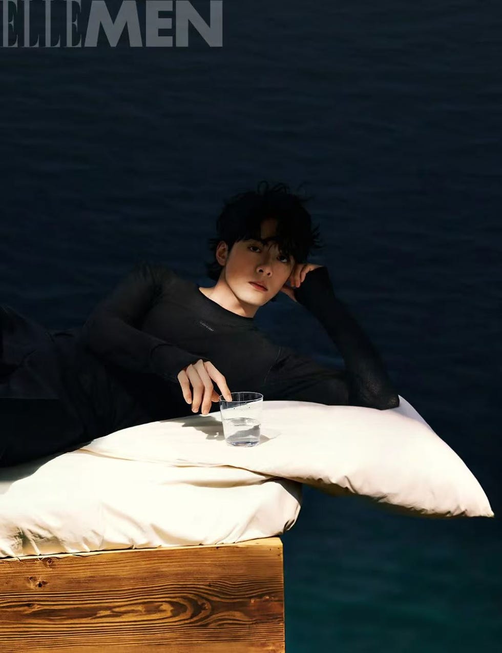 a person lounging on a wooden structure with a pillow and a clear cup of water