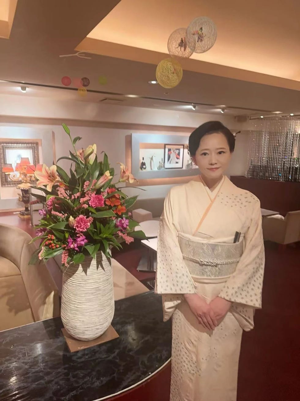 a woman in a traditional kimono stands beside a large floral arrangement