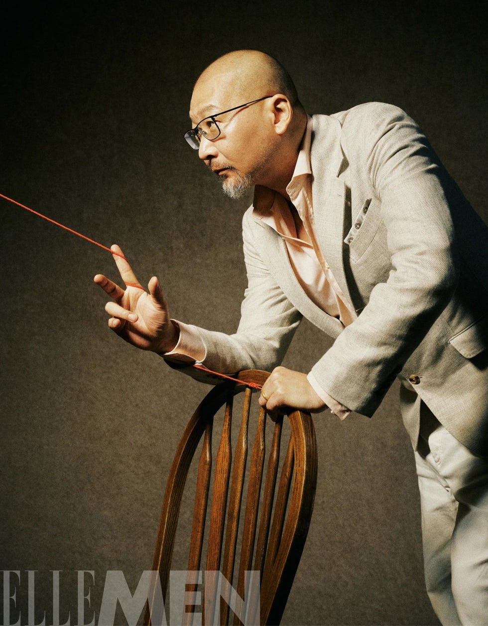 a man in a beige suit interacting with a chair and a red string