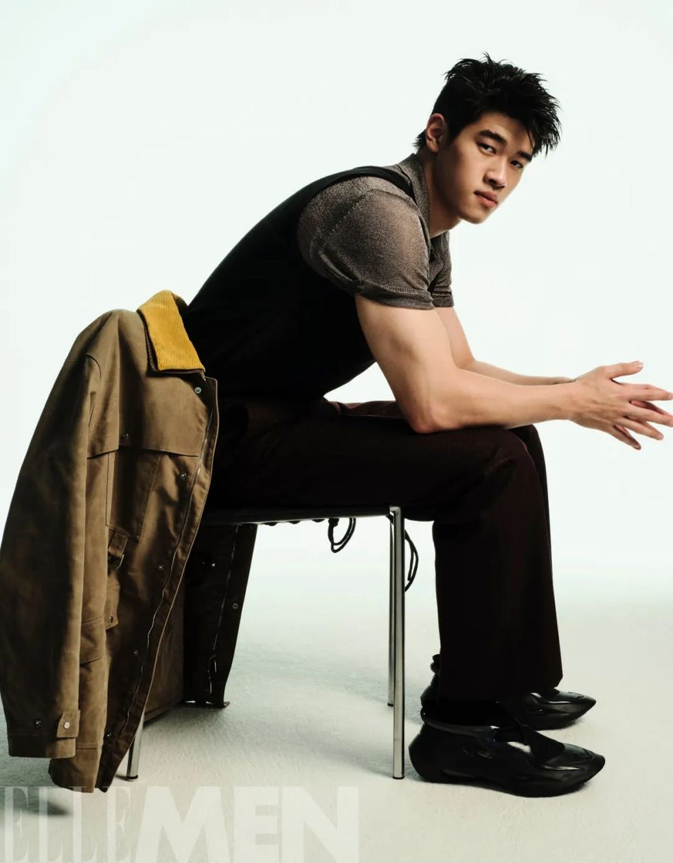 person sitting on a chair with a casual outfit and a coat draped over the chair