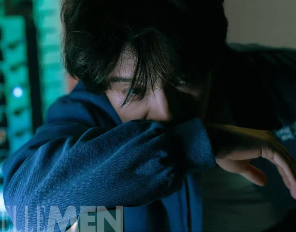 a person with a blurred face partially covering their face with their arm lit by a colored background