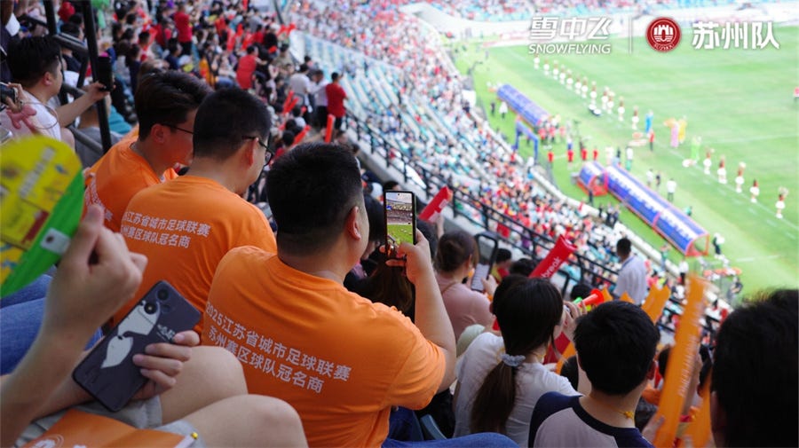 fans wearing orange shirts watching a football match in a stadium