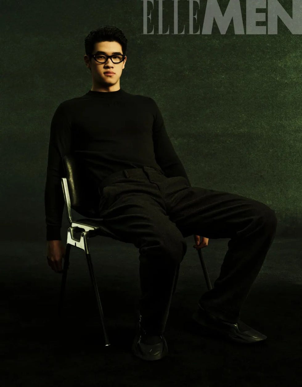 a seated figure wearing a black top and pants with a dark background