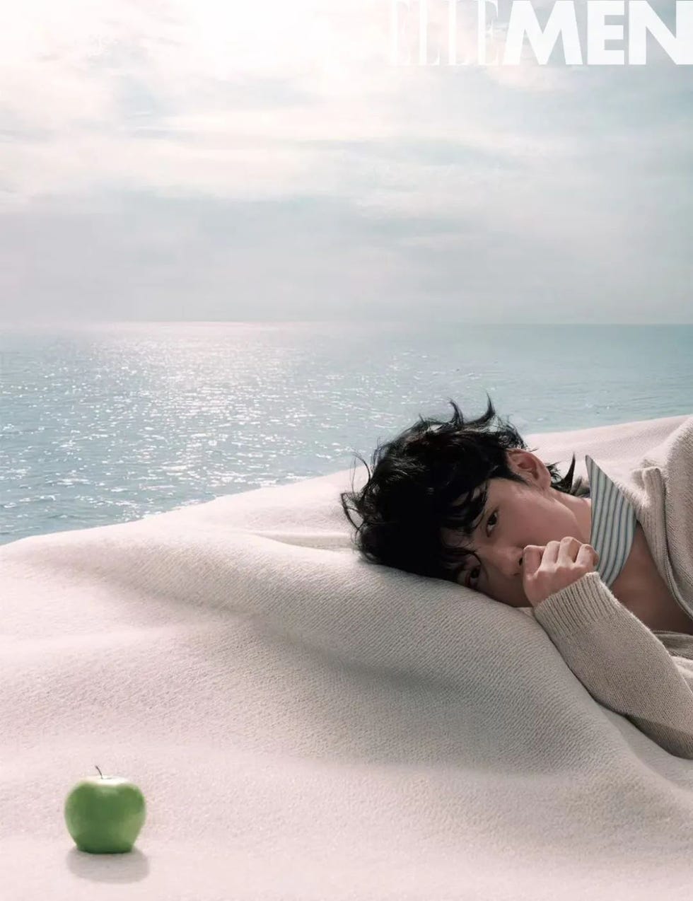 a serene scene by the sea featuring a person resting on a soft white surface with an apple nearby
