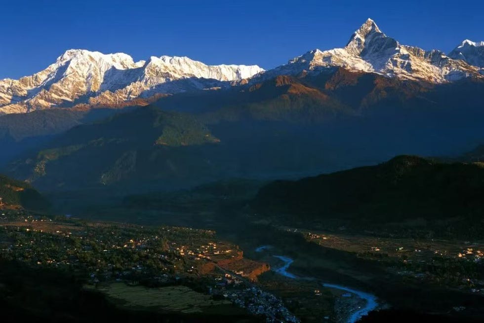 snowcapped mountain range with a valley and river below