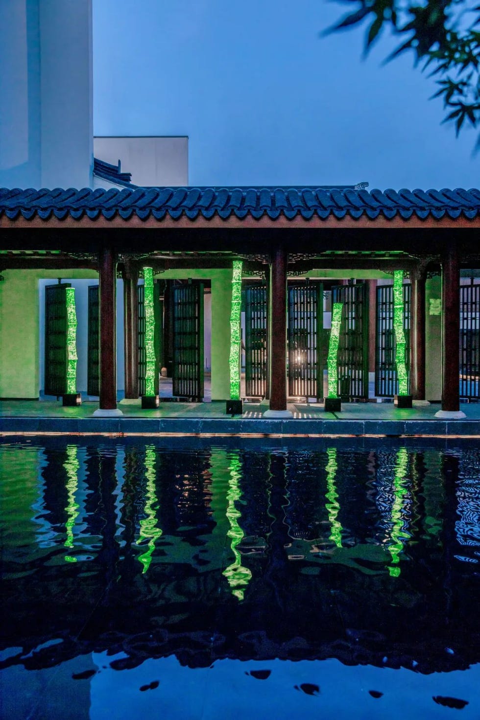 outdoor architectural space with illuminated green columns and a reflective water surface