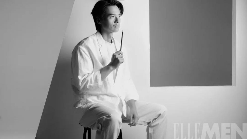 a seated individual holding a pencil in a minimalistic studio setting