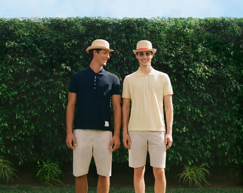two men standing side by side in stylish outfits against a green backdrop