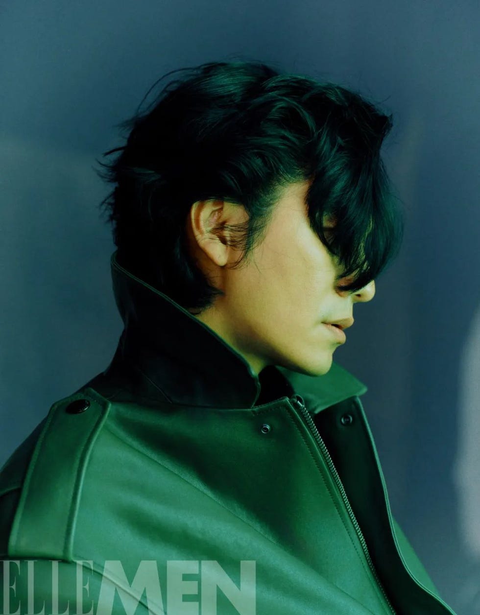 profile of a person wearing a green jacket against a blurred background
