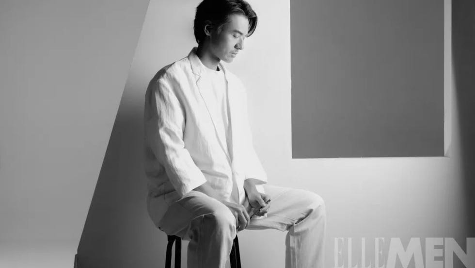 a seated individual wearing a lightcolored suit set against a geometric backdrop