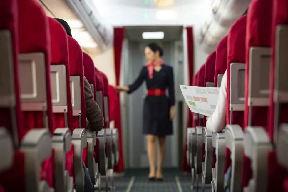 airplane interior with flight attendant in uniform and passenger holding a brochure