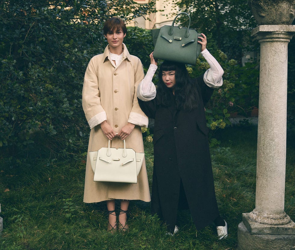 two individuals holding designer handbags in a garden setting
