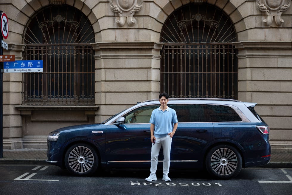 a person stands beside a luxury blue suv parked on a street
