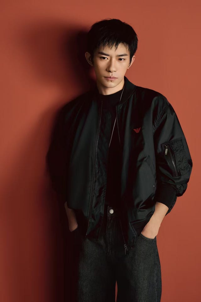 a person in a black bomber jacket against a terracotta background