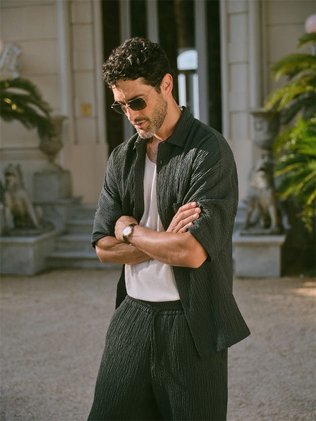 a man stands confidently with his arms crossed wearing casual clothing in an outdoor setting