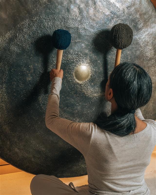 an individual playing a large gong with mallets