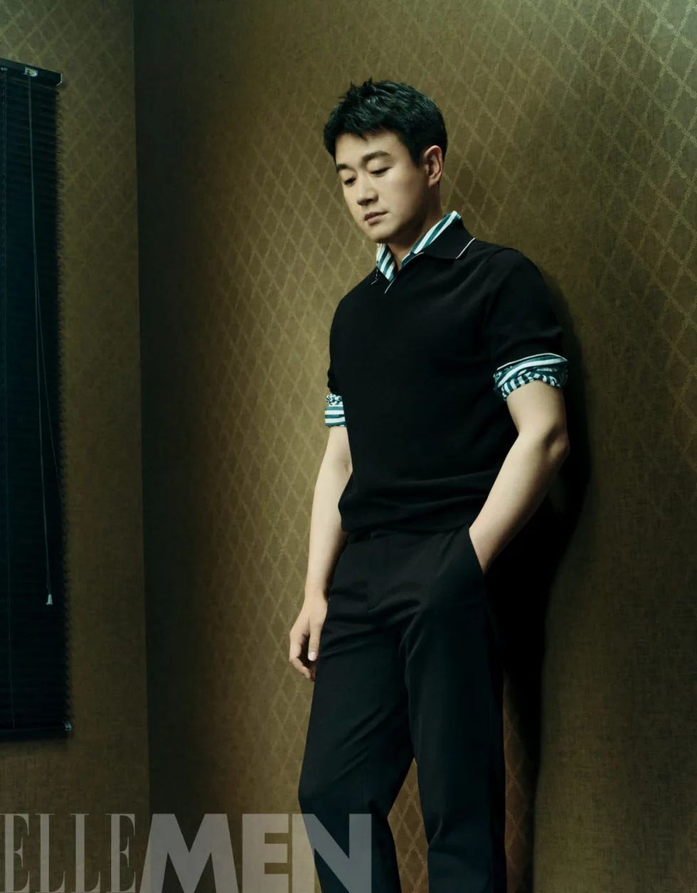 a casually posed individual dressed in stylish attire against a textured backdrop