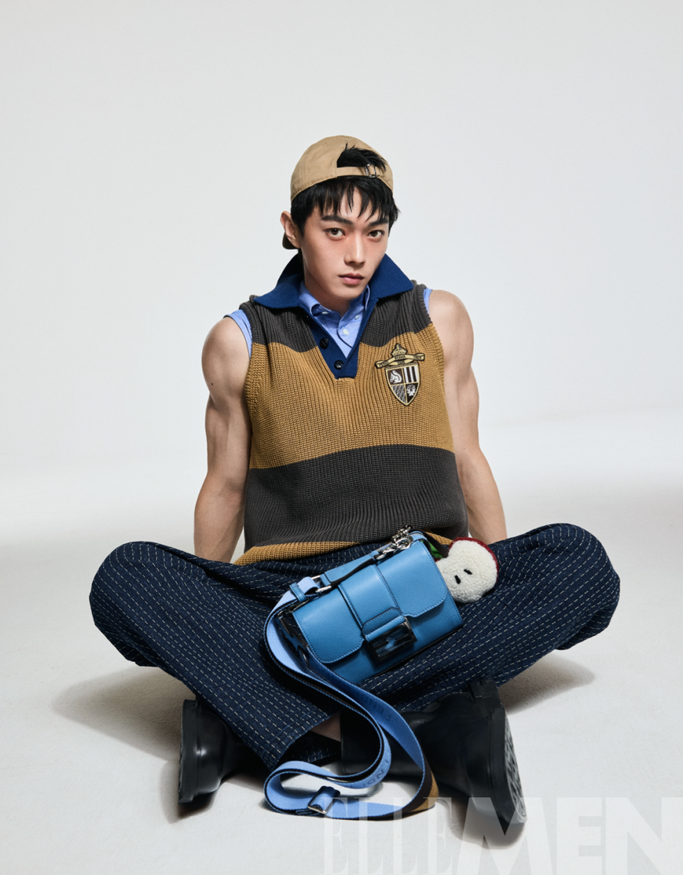 stylish individual sitting crosslegged wearing a colorblocked vest and patterned pants with a blue handbag