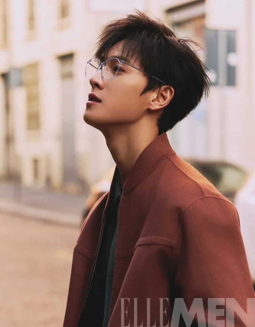 a person in a brown jacket stands against a blurred urban background