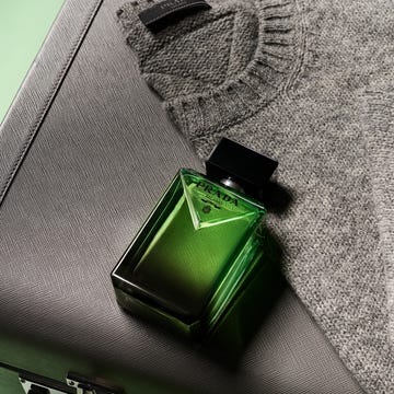 prada fragrance bottle displayed with a gray sweater and a textured black case prada fragrance bottle displayed with a gray sweater and a textured black case